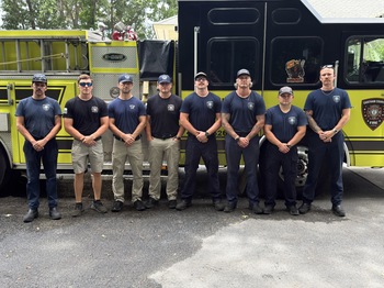Eight firefighters standing in front of an engine