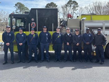 Nine firefighters in front of a fire truck posing in a group picture