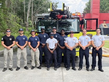 10 firefighters standing in a row in front of a ladder truck