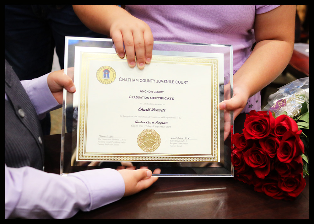 A bouquet of roses lies beside an Anchor Court graduation certificate in the hands of a graduate's children.