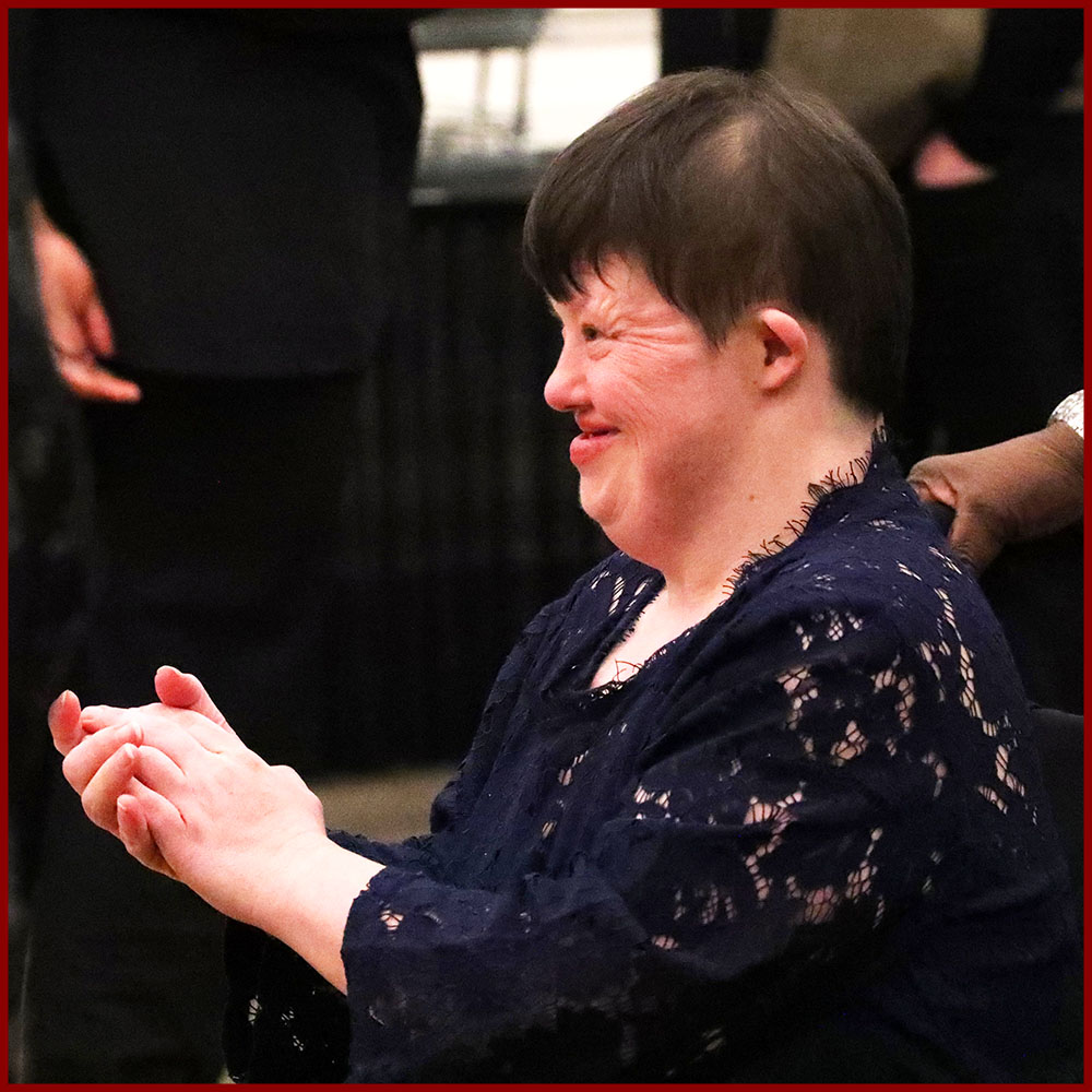 elegantly dressed woman with downs syndrome smiles and applauds at holiday ball